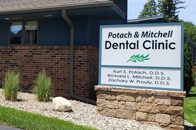 Potach & Mitchell Dental Clinic exterior sign with brick building and landscaping.