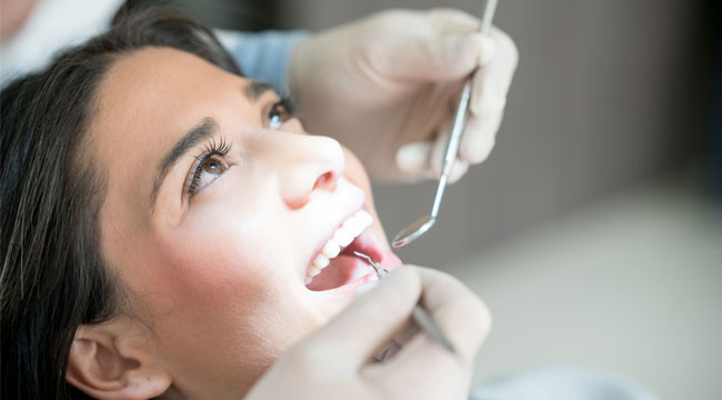 Woman receiving dental examination by dentist wearing protective eyewear in clinical setting.