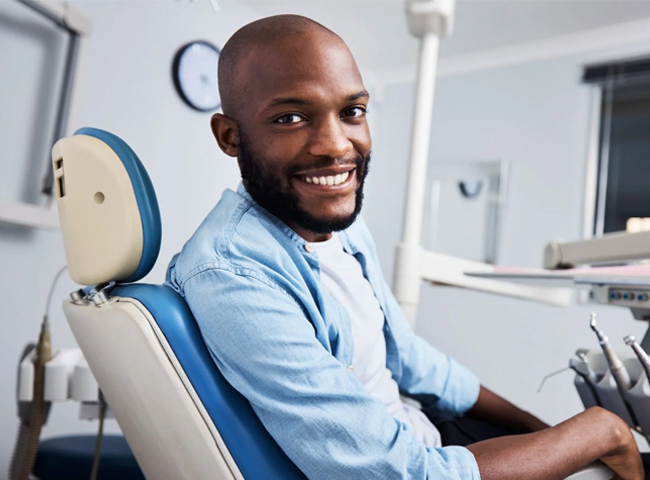 Smiling male dentist in blue shirt seated in modern dental office clinic setting.