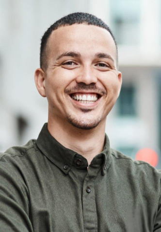 Smiling male dental professional in olive shirt against blurred clinic background.
