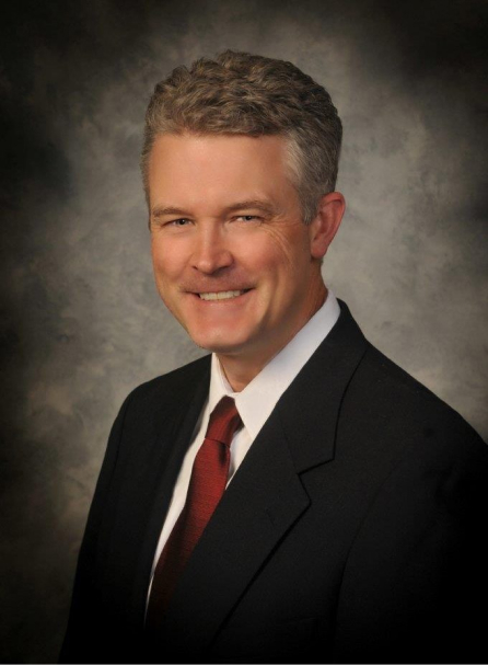 Professional headshot of male dentist in business suit against neutral studio background.