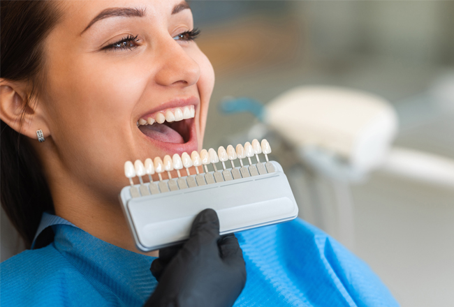 Woman smiling while holding dental shade guide at dental clinic during consultation.