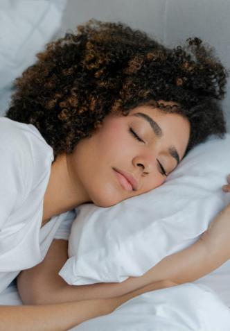 Woman sleeping peacefully on white pillow and bedding, demonstrating rest and wellness.