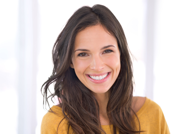 Professional headshot of smiling woman in yellow shirt against white background for dental clinic.