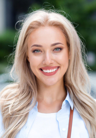 Professional headshot of smiling woman with blonde hair in white shirt at dental clinic.