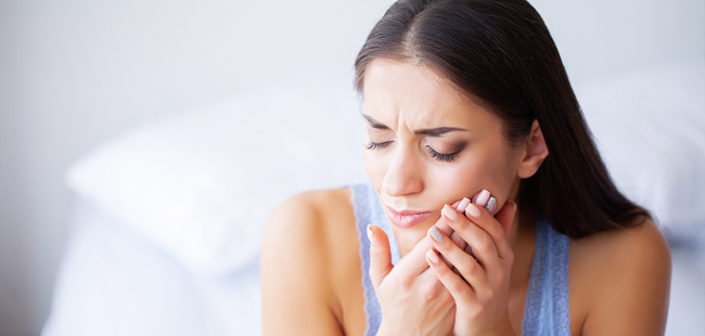 Woman experiencing tooth pain, holding her cheek while sitting indoors