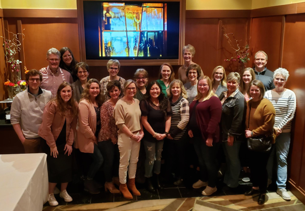 Large group of dental clinic staff posing together in formal indoor setting.